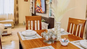 Un comedor con una mesa de madera dispuesta para cuatro, un jarrón con plumas blancas y un televisor al fondo.