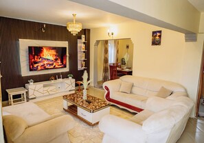 A modern living room with a flat-screen TV, white sofas, a coffee table, and a fireplace. - Welcome to your perfect getaway! This stunning 3-bedroom house, located in Thika (Thika)