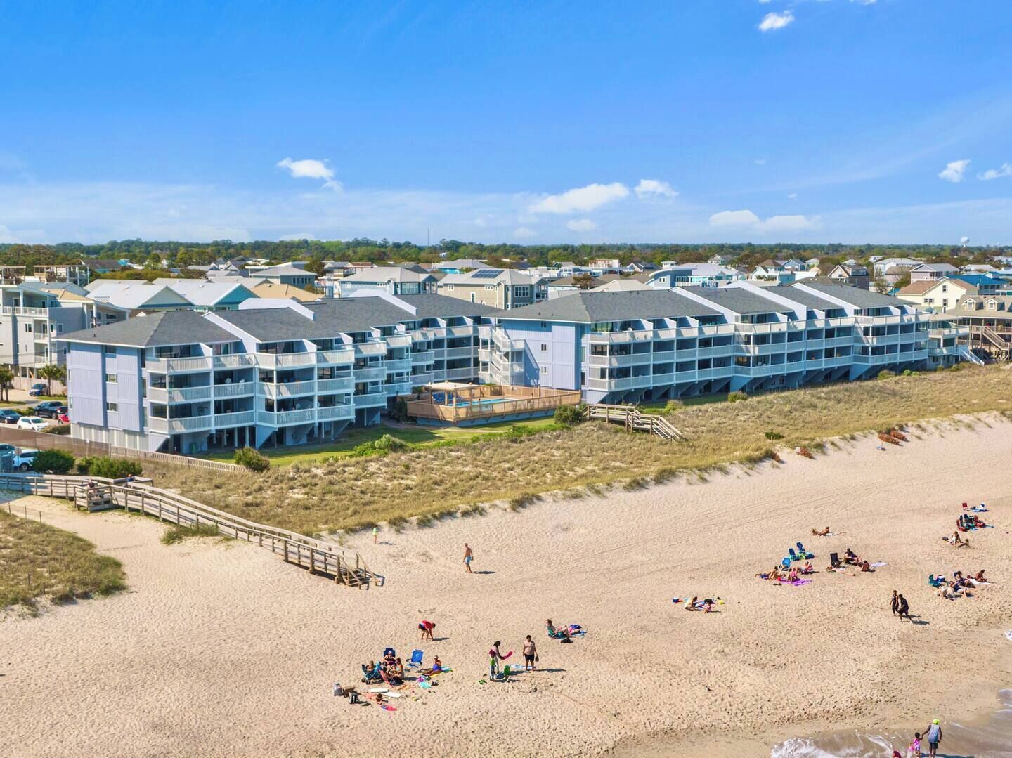 Ein Strandhotel mit mehreren Balkonen, einem Sandstrand und blauem Himmel.