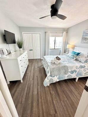 A bedroom with a bed, a desk, a ceiling fan, a TV, and a window with curtains. - Top Floor Beachfront w Pool & Ocean Sunrise Views! (Carolina Beach)
