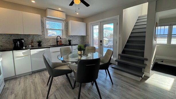 A modern kitchen with white cabinets, a black countertop, and a glass dining table with four chairs. - Unwind at Windemere 3-Bedroom Apartment in Thunder Bay (Thunder Bay)