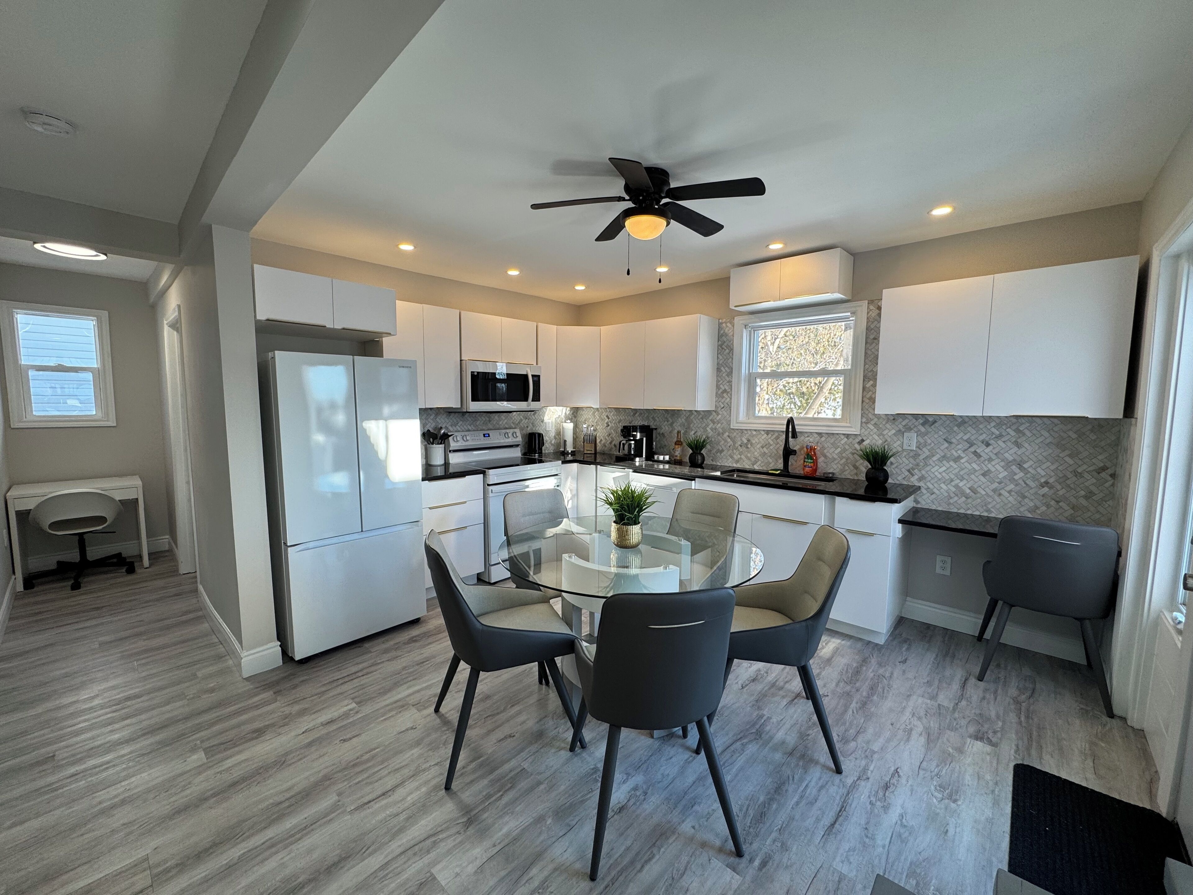 A modern kitchen with white cabinets, a black countertop, and a glass dining table surrounded by chairs.