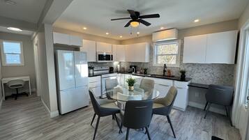 A modern kitchen with white cabinets, a black countertop, and a glass dining table surrounded by chairs.