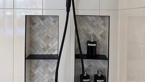 A modern shower with a handheld attachment, a control panel, and a storage shelf with bottles of shampoo and conditioner. - Unwind at Windemere 3-Bedroom Apartment in Thunder Bay (Thunder Bay)