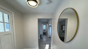 A hallway with a white door, a black mat, a round mirror, and a ceiling light. - Unwind at Windemere 3-Bedroom Apartment in Thunder Bay (Thunder Bay)