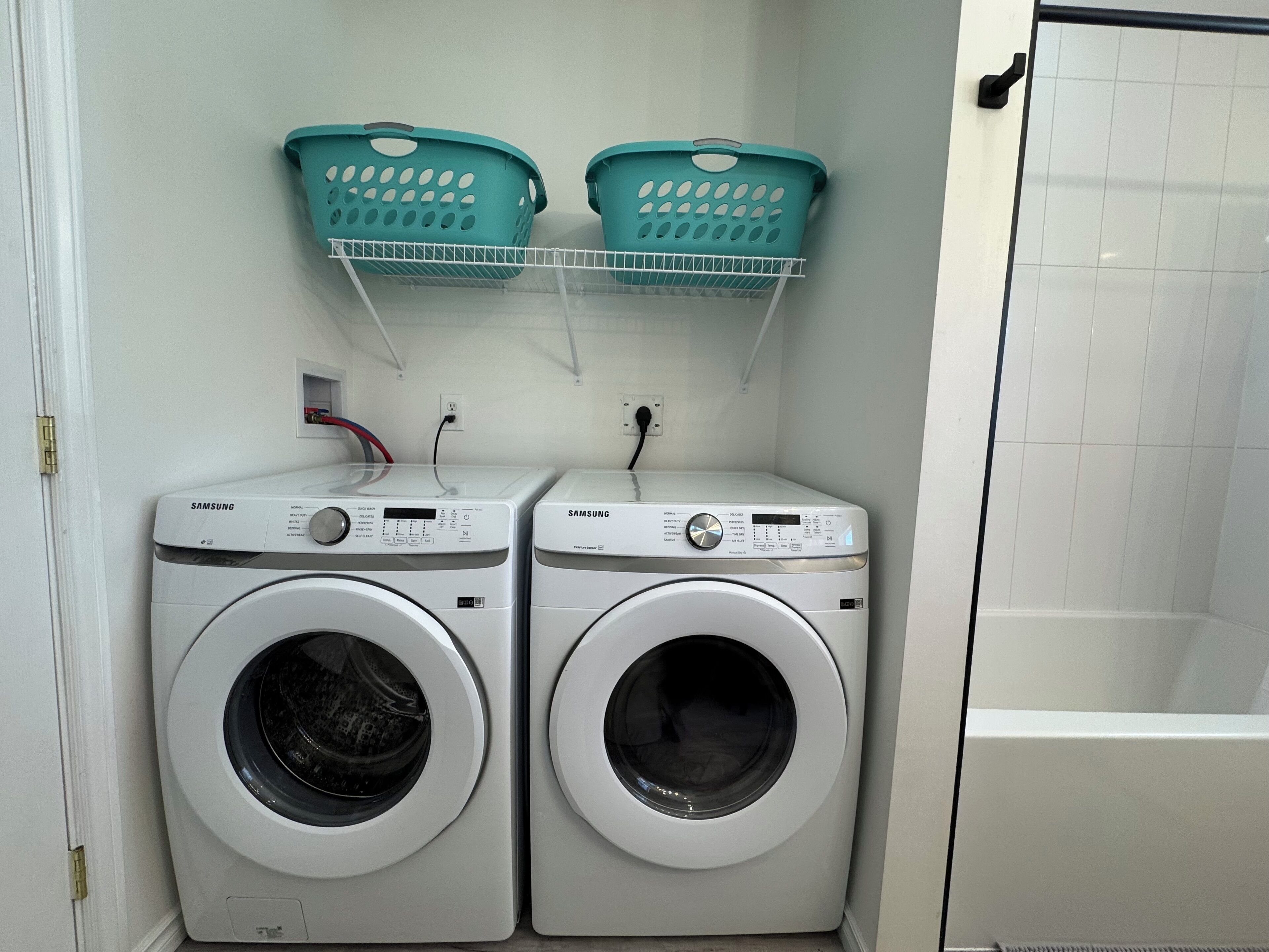 Un área de lavandería con dos lavadoras Samsung y dos cestos teal sobre un estante blanco.