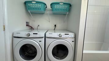 Un área de lavandería con dos lavadoras Samsung y dos cestos teal sobre un estante blanco.