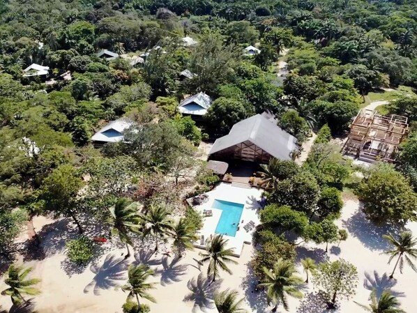 An aerial view of a resort with multiple bungalow-style accommodations surrounded by dense tropical vegetation.