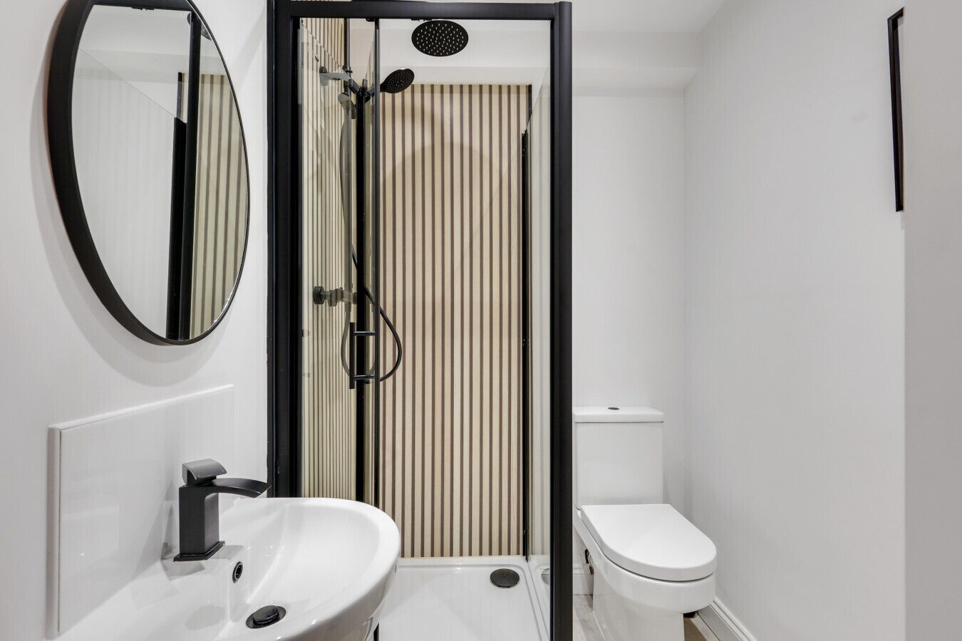 A modern bathroom with a white sink, toilet, and a shower enclosure with vertical blinds.
