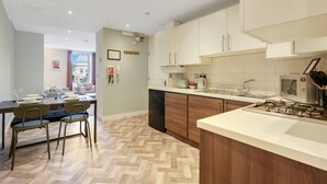 Uma cozinha moderna com armários de madeira, uma ilha central e uma área de jantar com padrão de piso em herringbone.