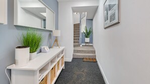 Um corredor com um console branco, uma luminária e uma planta. Escada leva a outro nível.