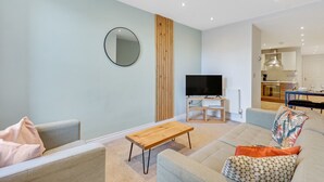 Uma sala de estar moderna com uma TV de tela plana, uma mesa de centro de madeira e um sofá com almofadas estampadas.