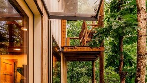 Eine Holzterrasse mit Glastür, die zu einem Raum führt, umgeben von Bäumen.