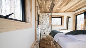 Ein Schlafzimmer mit Holzboden, einem Bett mit weißer Bettwäsche und einem jalousieförmigen Insektenschutznetz.