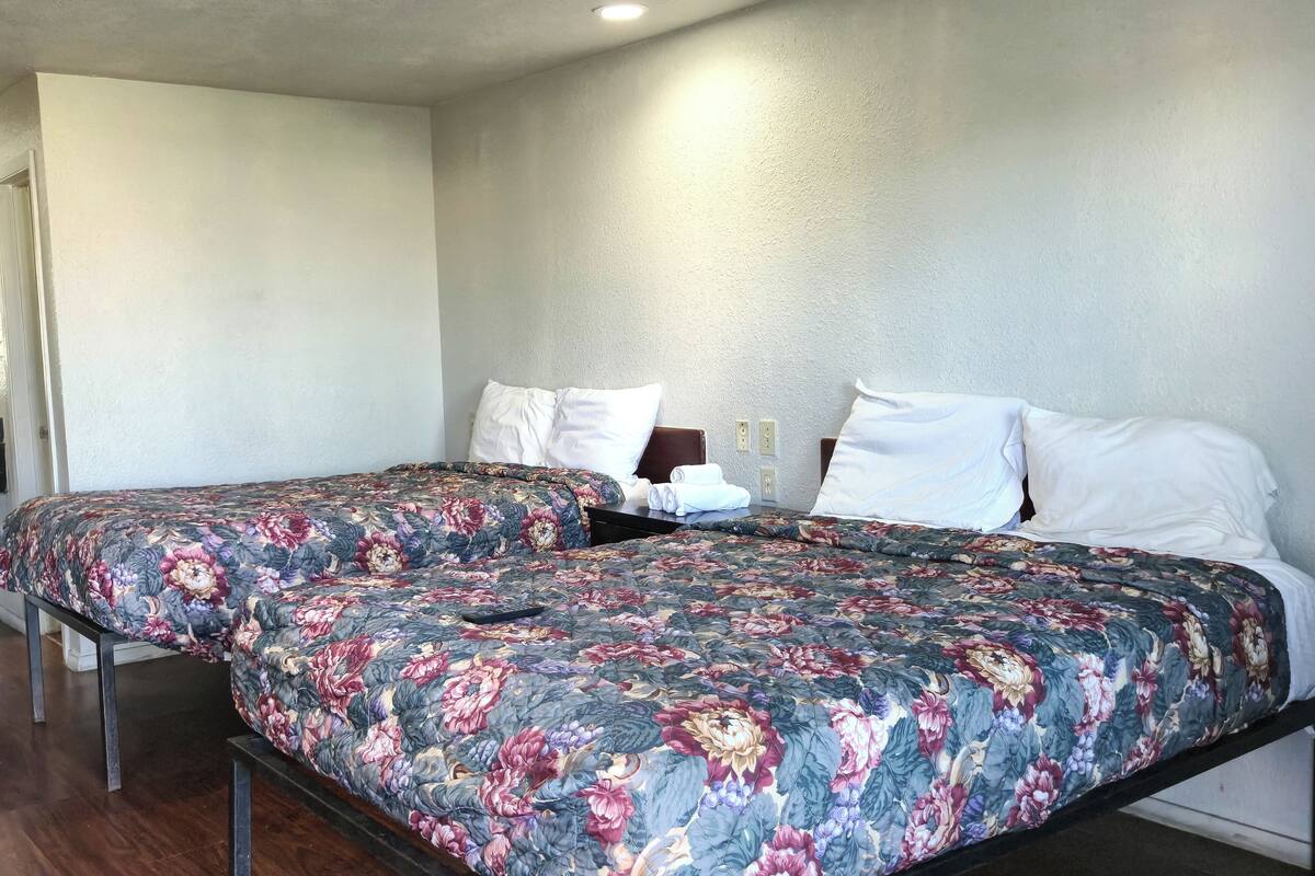 Uma cama de casal com roupa de cama florida, uma mesa de cabeceira e um candeeiro fixado na parede.