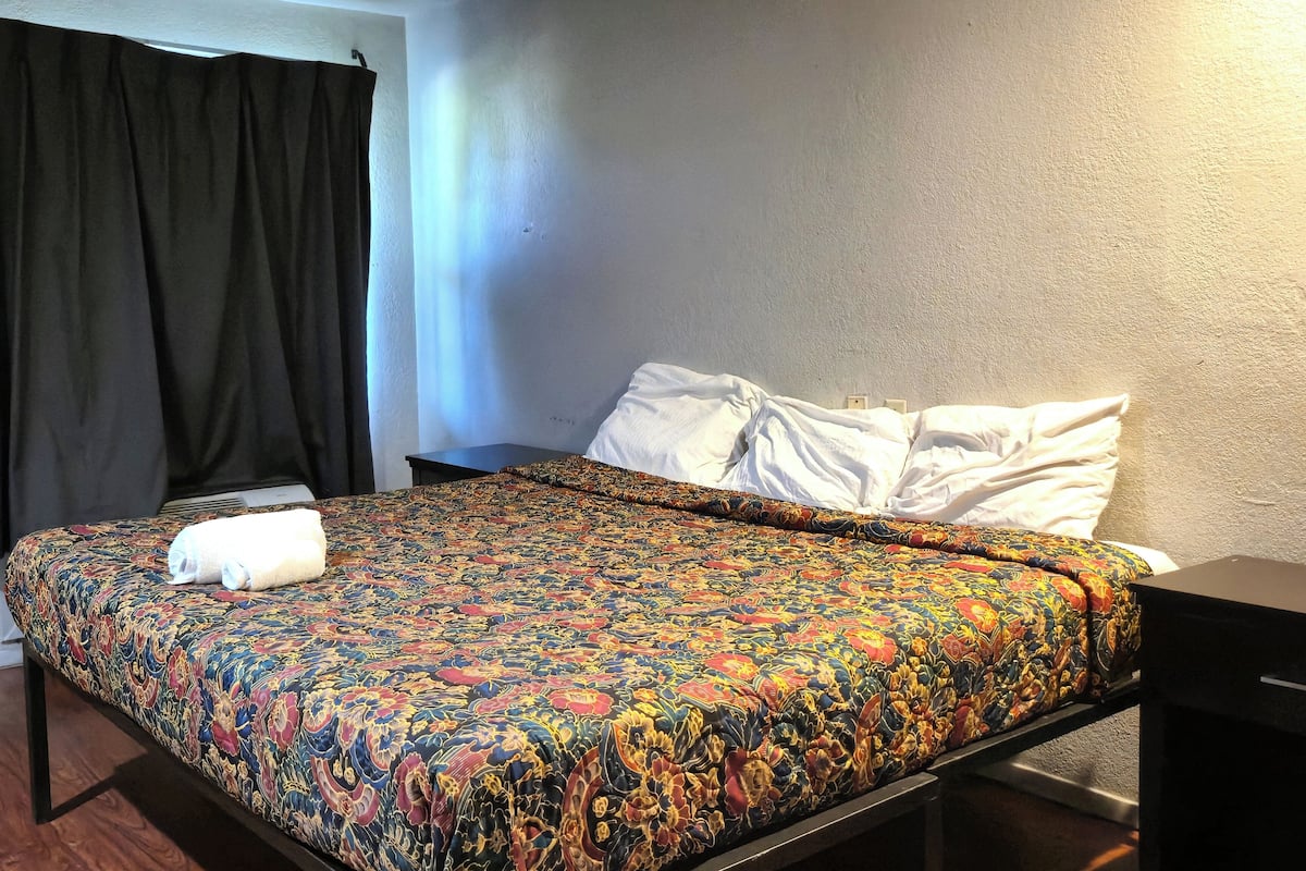 Uma cama com um edredom colorido estampado, um travesseiro branco e uma toalha dobrada.