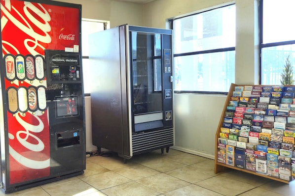 A vending machine with a Coca-Cola logo, a vending machine with a glass door, and a book display stand. - Deluxe Inn Motel By Oyo Grand Prairie Interstate 30 (Grand Prairie)