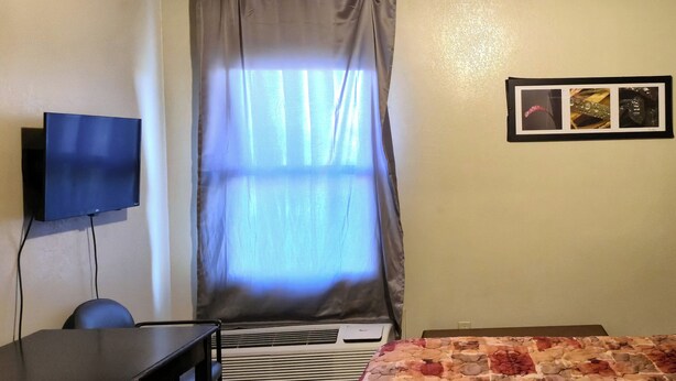 A hotel room with a bed, a desk, a television, an air conditioning unit, and a window with curtains. - Cole Manor Motel By OYO Love Field Market Center (Dallas)