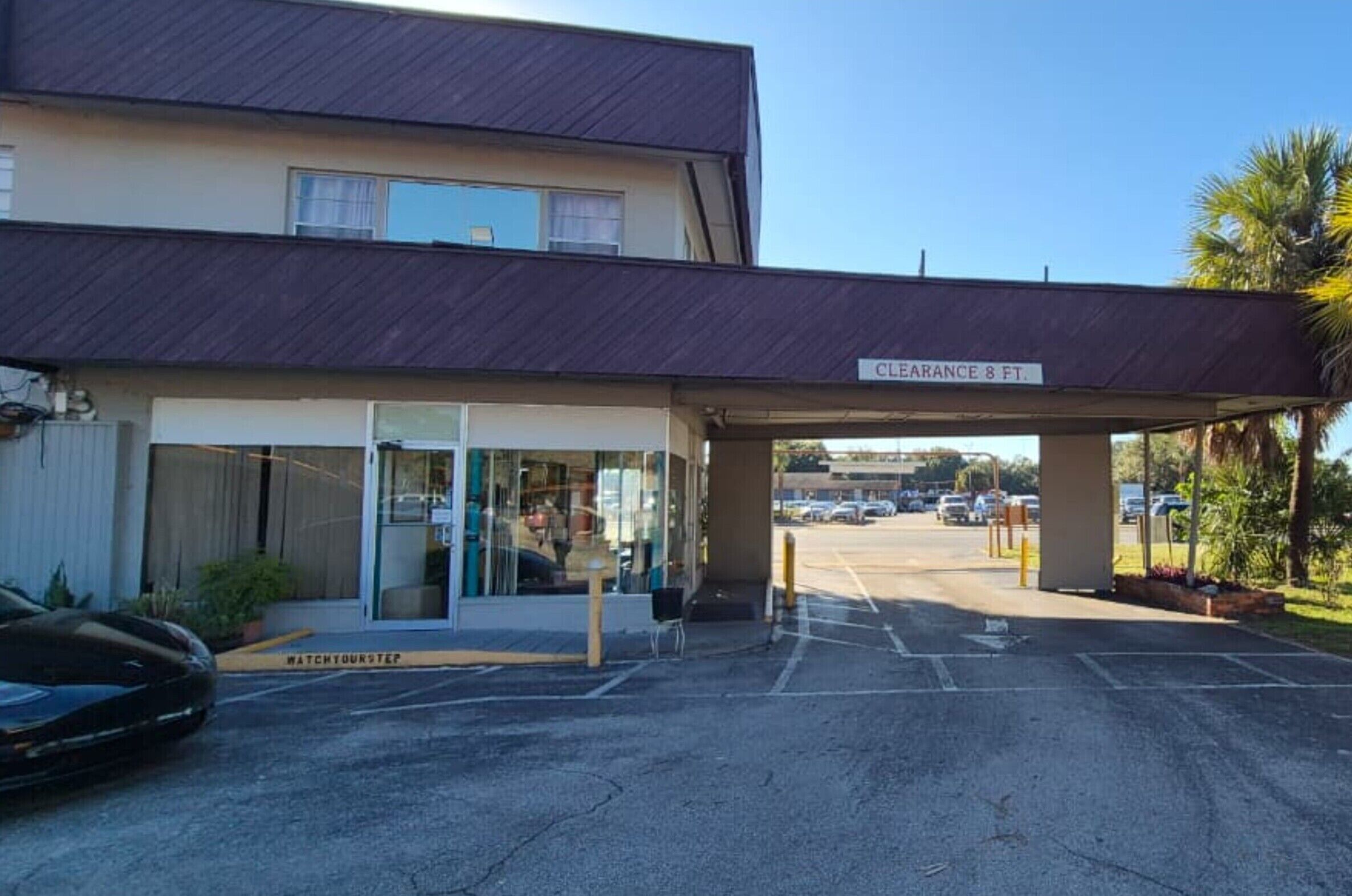 A hotel entrance with a covered walkway, a sign indicating a clearance of 8 feet, and a parking lot with cars.