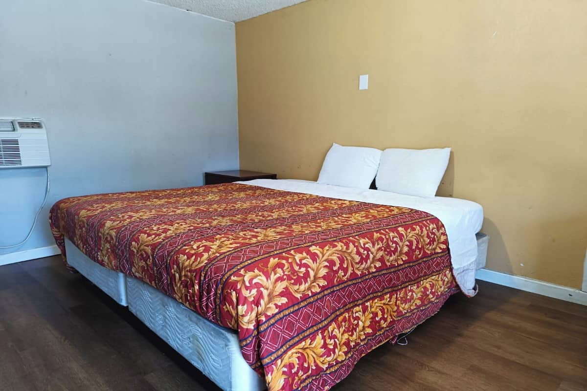 A hotel room with a large bed, a nightstand, and an air conditioning unit on the wall.