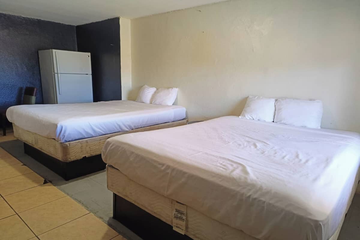 Two single beds with white linens in a room with a refrigerator and a tiled floor.