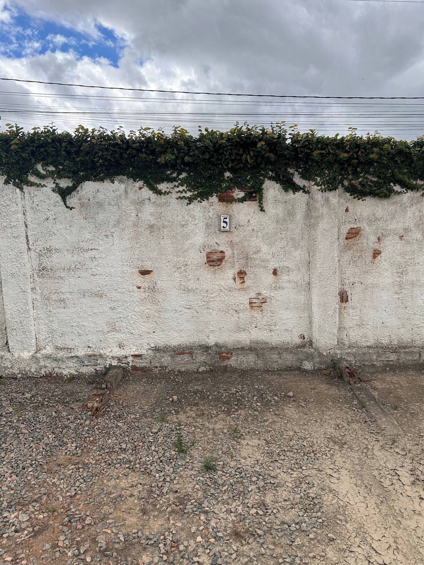 A concrete wall with a number '5' sign, surrounded by gravel and sparse vegetation.
