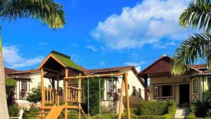 A playground with a slide and swings, surrounded by well-maintained grass and palm trees, with houses in the background. - Beautiful and cozy house! (Novo Gravatá Gravatá)