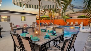 Un espace repas aménagé au bord de la piscine, avec une table dressée pour quatre personnes, entourée de chaises, et un flotteur gonflable en forme de cygne.