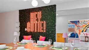 Un espace repas agrémenté d’un néon, une table dressée pour six personnes et une fresque murale colorée en arrière-plan.