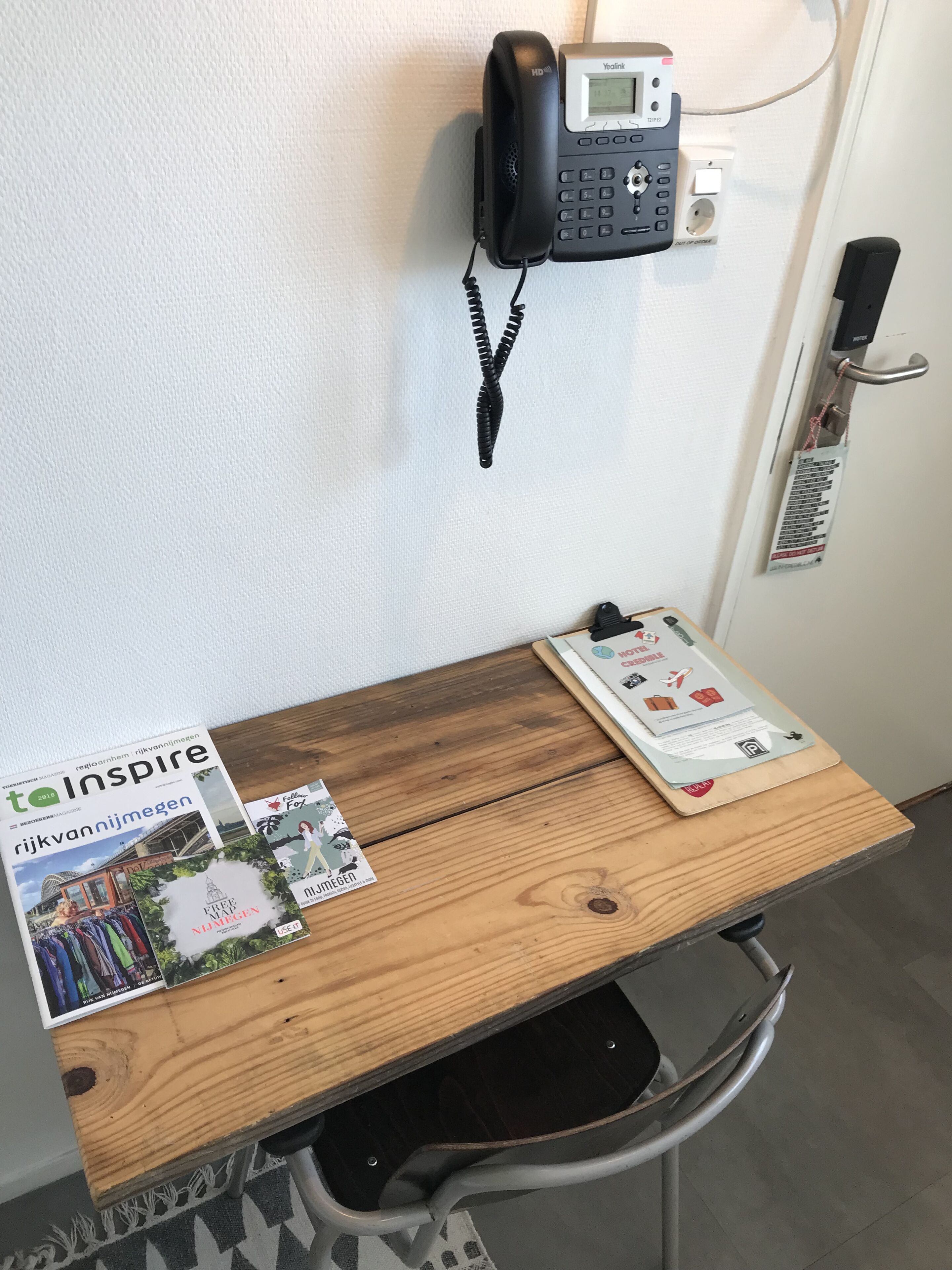 Una mesa de madera con una revista, un teléfono y una puerta con un cartel.