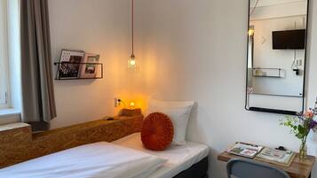 Une chambre d’hôtel comprenant un lit, une table de chevet, une lampe, un miroir et un petit bureau avec une chaise.