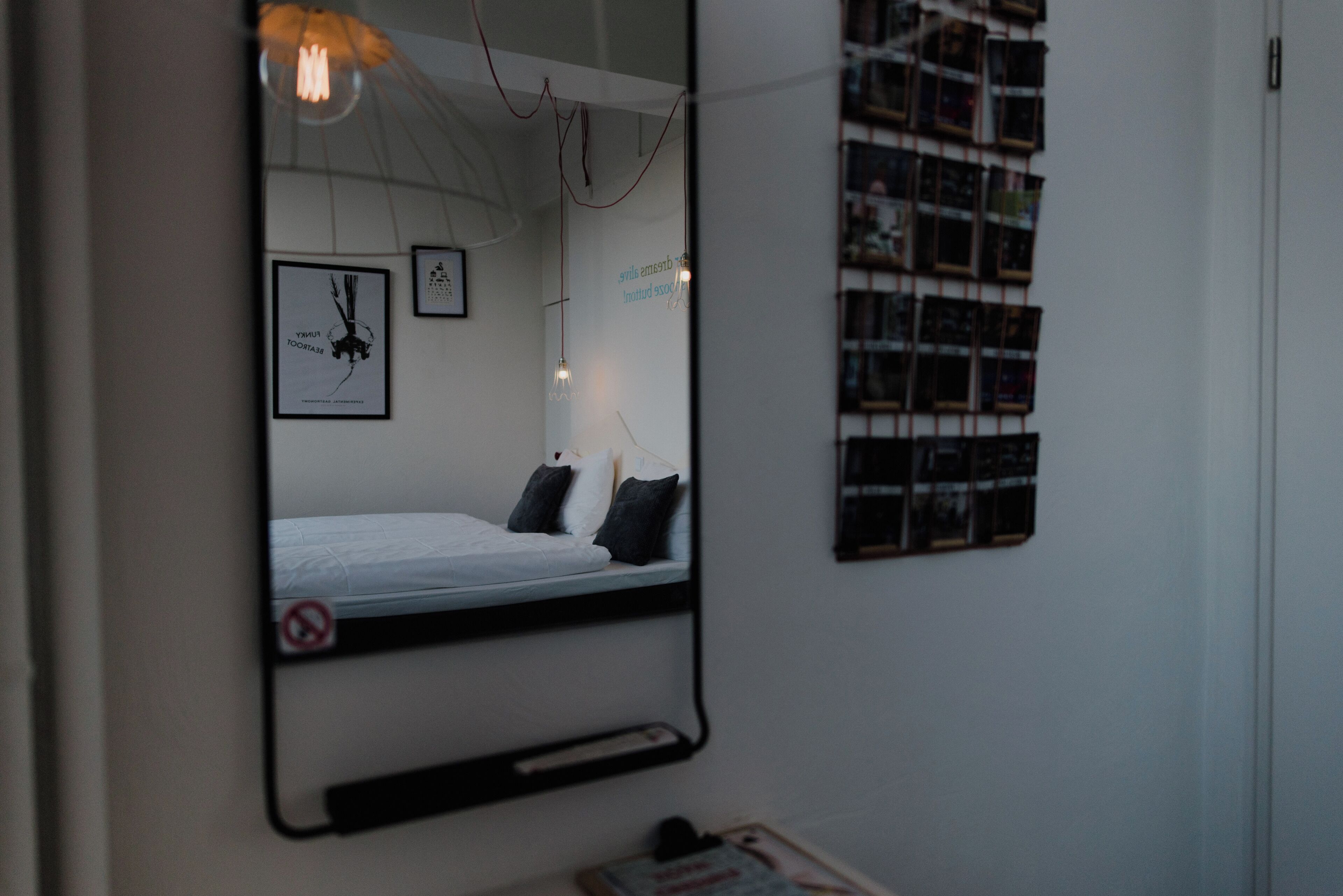 A bedroom with a bed, a mirror, a wall-mounted light fixture, and a framed picture.
