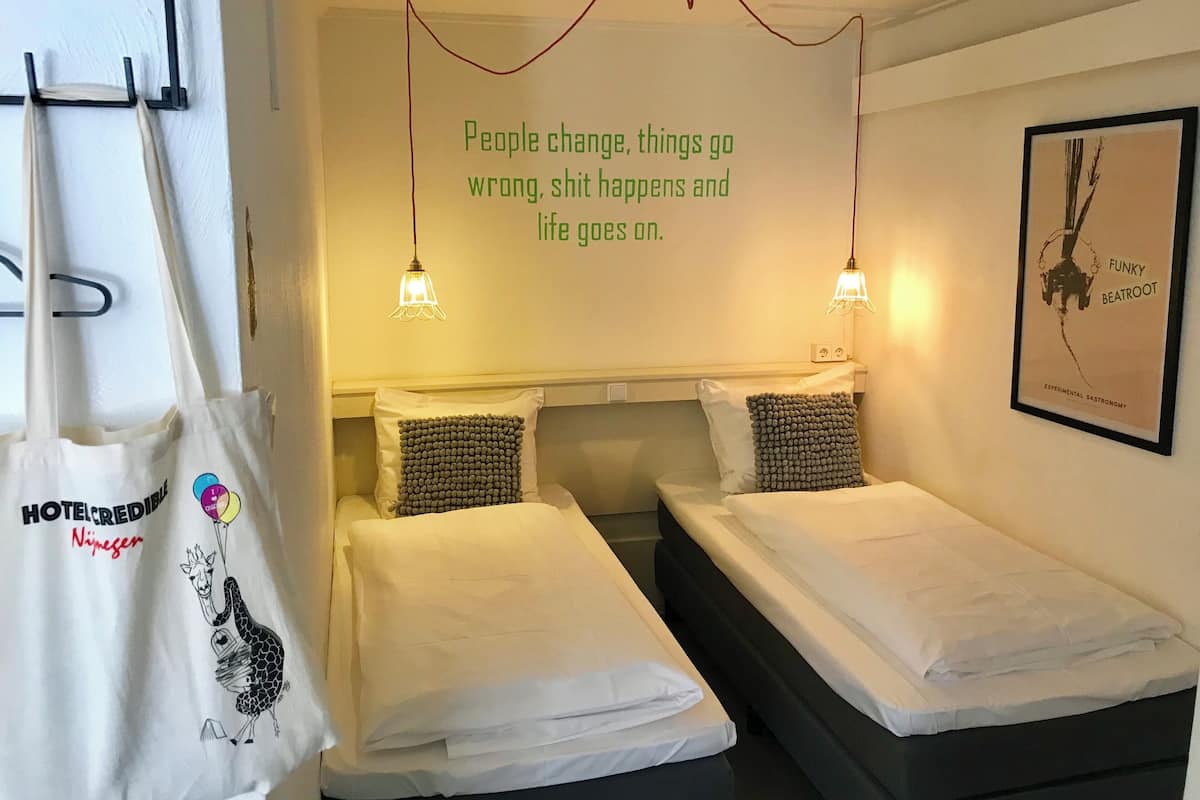 A hotel room with two beds, a wall-mounted light fixture, a framed poster, and a hanging bag.
