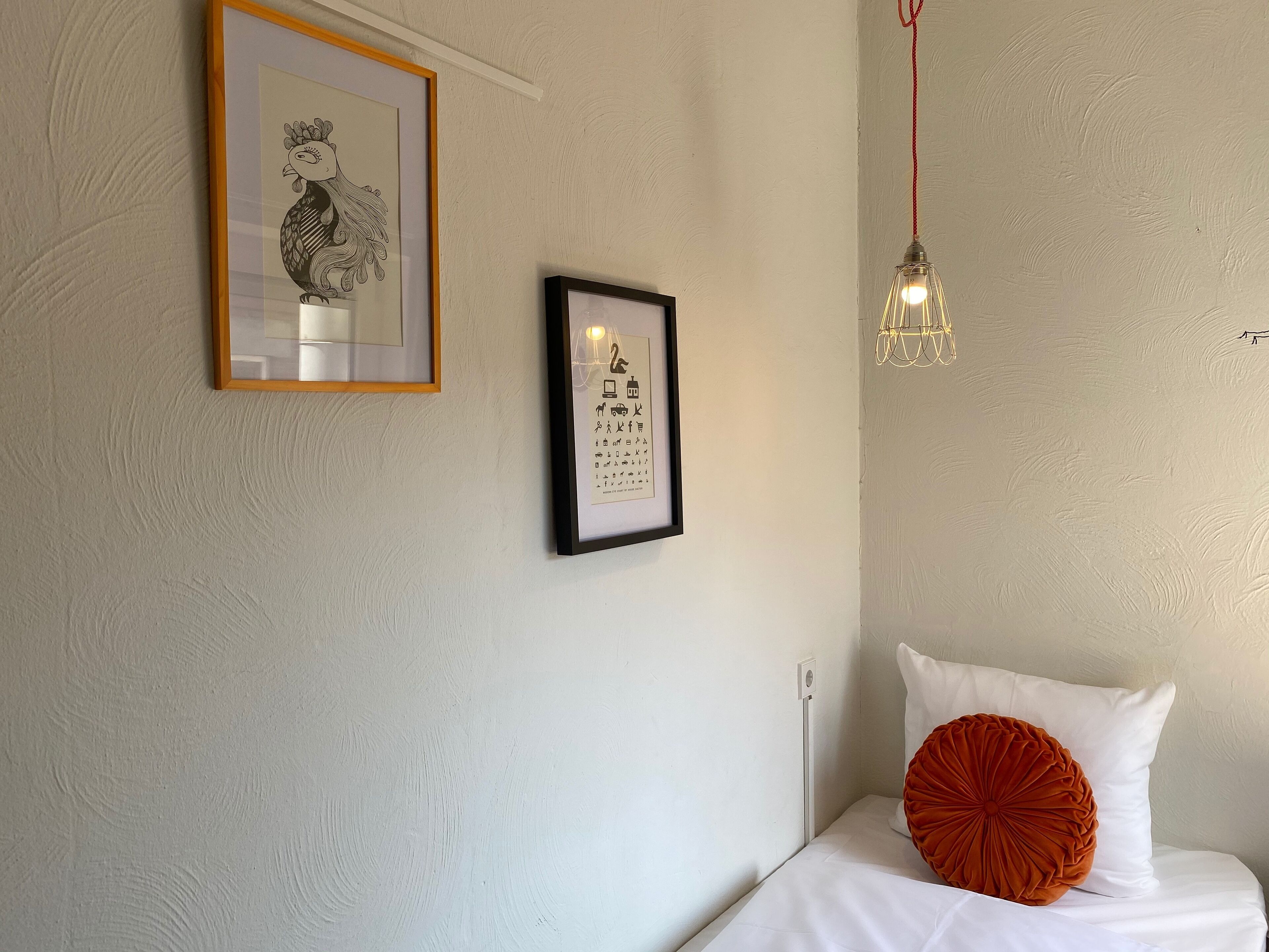 Une chambre à coucher avec un lit, une œuvre d’art encadrée, un luminaire fixé au mur et un mur blanc.