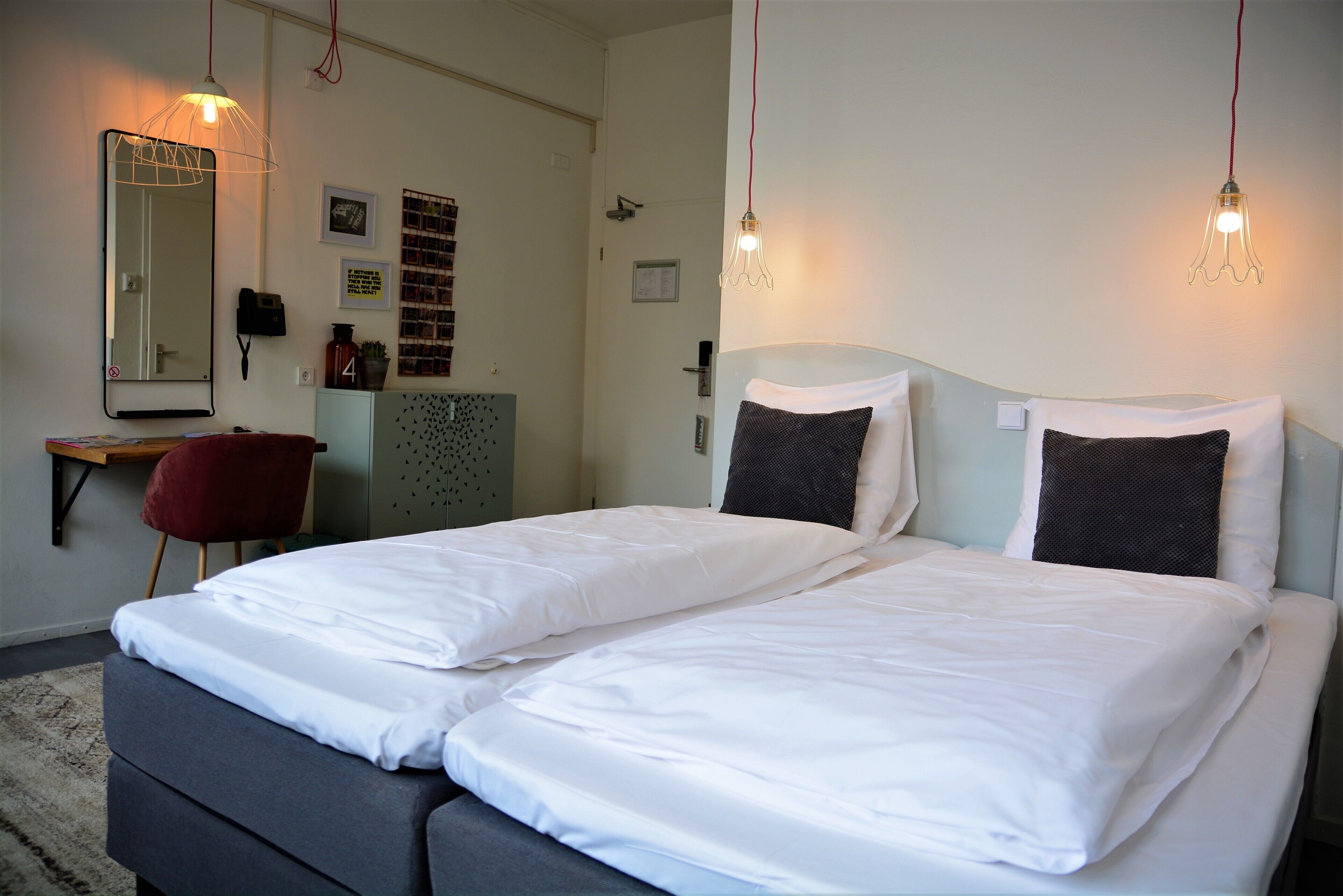 Ein Doppelbett mit weißen Leinen, ein roter Sessel, ein Schreibtisch mit Spiegel und Wandleuchten.