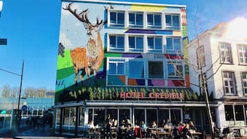 Ein Hotel mit einem farbenfrohen Wandgemälde von einem Reh an der Seite, Außenbestuhlung und blauem Himmel.