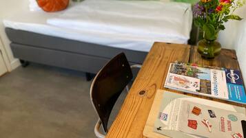 Una camera da letto con un letto, un tavolo in legno con brochure, una sedia e un vaso con fiori.