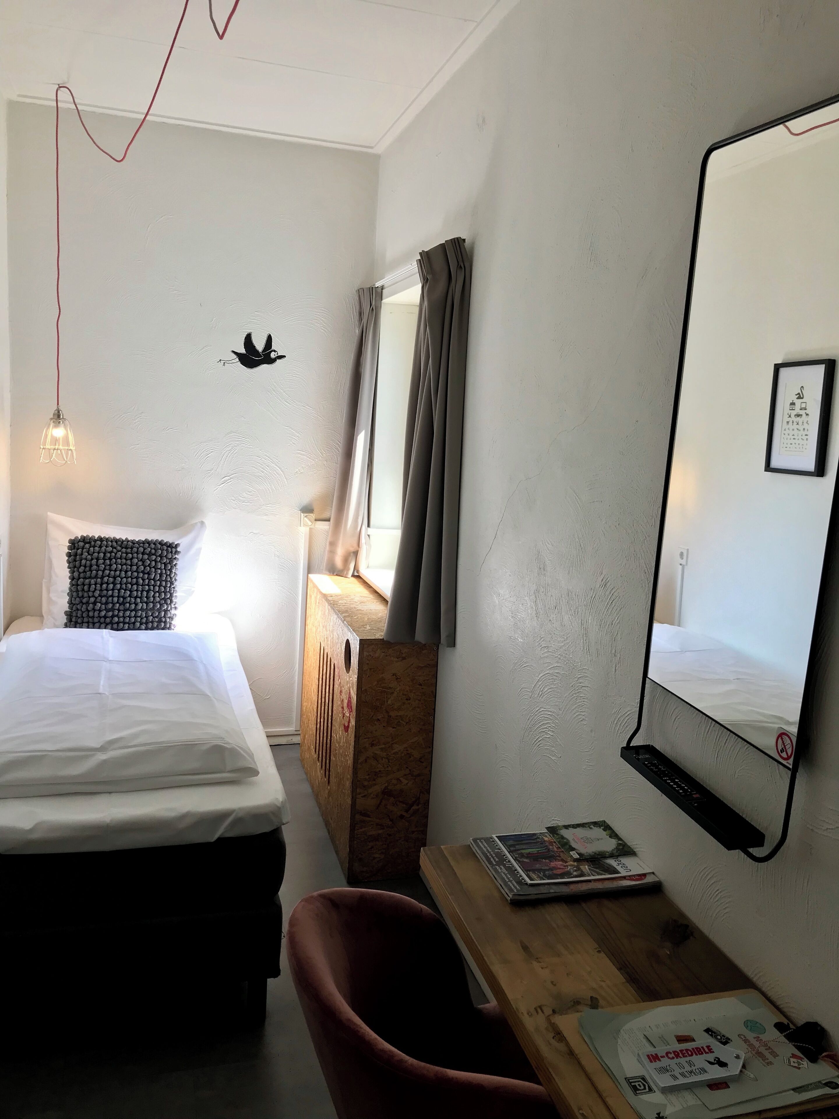 A hotel room with a bed, a desk, a chair, a mirror, and a wall-mounted TV.