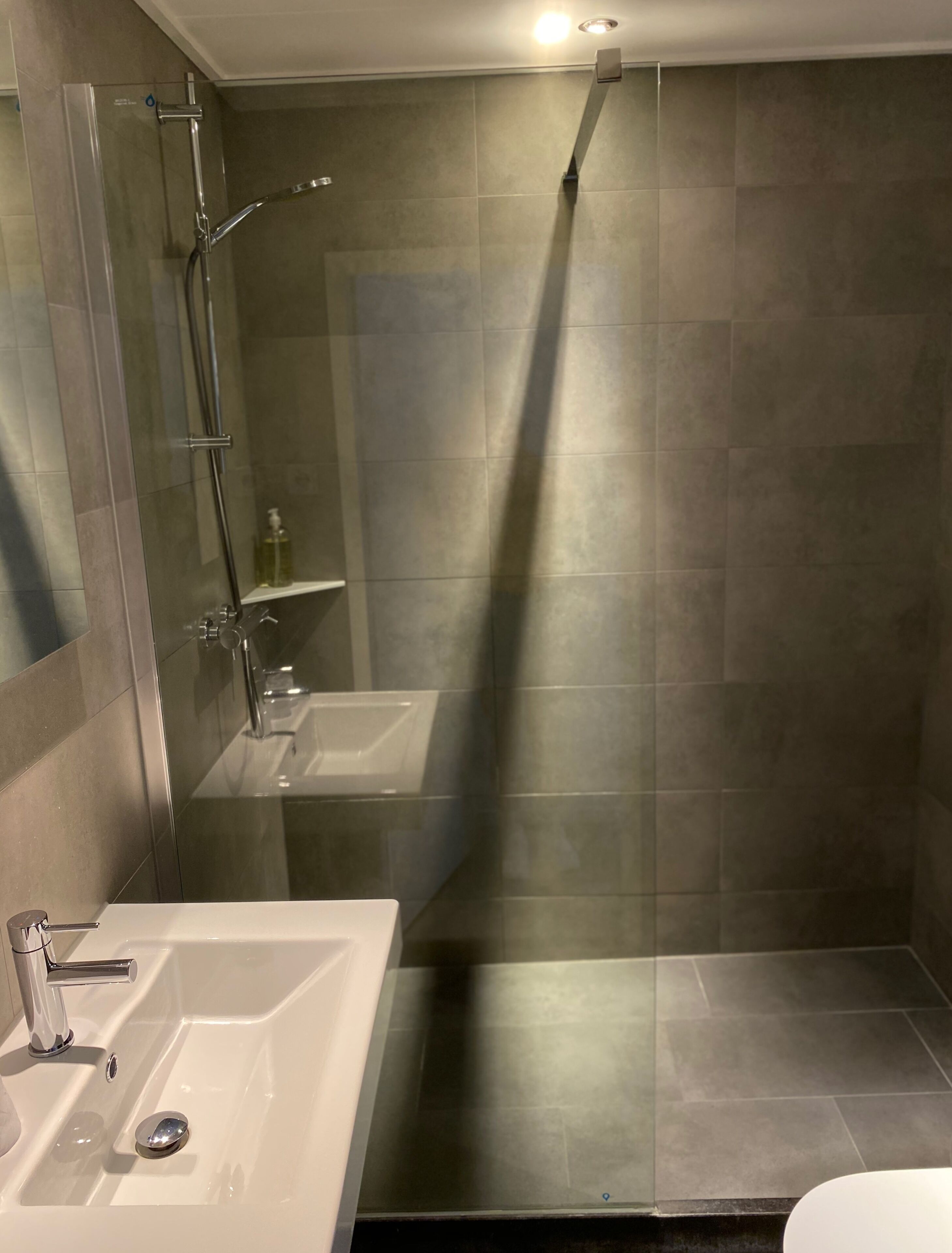 A modern bathroom with a glass-enclosed shower, a white sink, and a mirror.