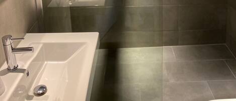 A modern bathroom with a glass-enclosed shower, a white sink, and a mirror.