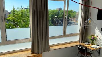A room with large windows, a wooden desk, a chair, a radiator, and a hanging light fixture.