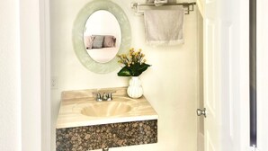 Une salle de bain avec un meuble-lavabo en bois, un miroir rond, un porte-serviettes avec des serviettes et une petite plante en pot.