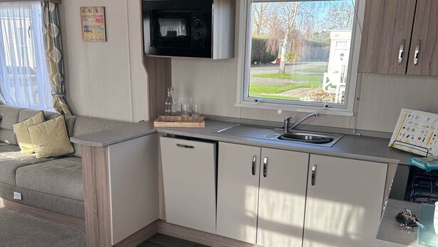 Eine kompakte Küchenzeile mit Mikrowelle, Spüle und Schränken, ein Fenster mit Blick auf ein Wohngebiet und ein Sofa mit Kissen.