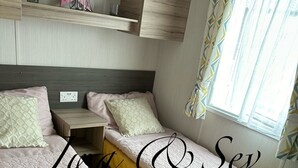 Ein Hotelzimmer mit zwei Betten, einem kleinen Tisch, einer Ablage mit Dekoration und einem Fenster mit Vorhängen.
