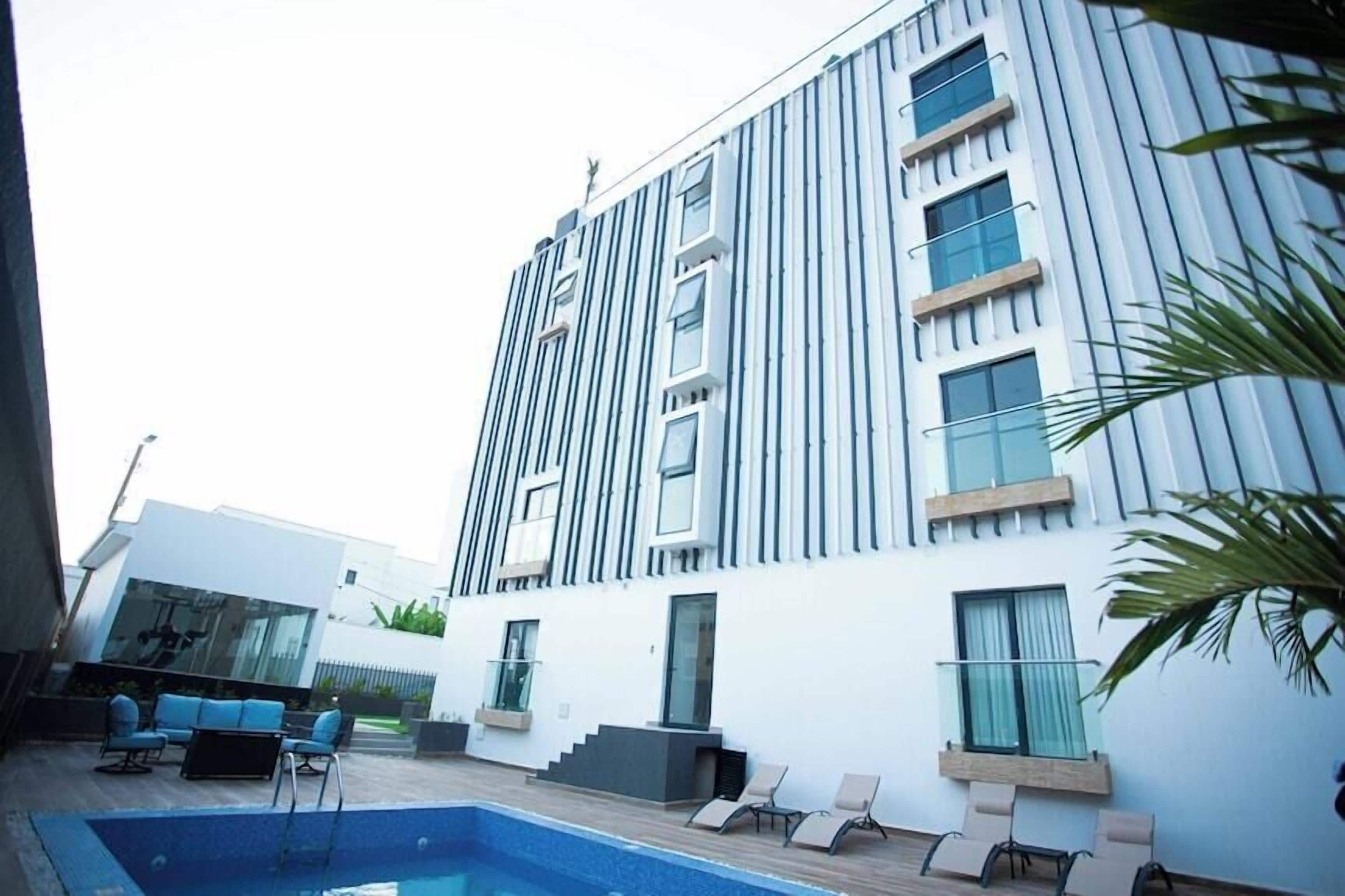 A modern building with a pool area, including lounge chairs and a glass balustrade.