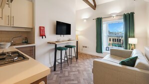 Cocina moderna con estufa a gas, televisión de pantalla plana y un taburete de bar. Cuenta con un sofá y una ventana con cortinas, que ofrece vistas de la ciudad.