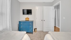 Un dormitorio con dos camas, un aparador azul, un televisor y una puerta blanca.