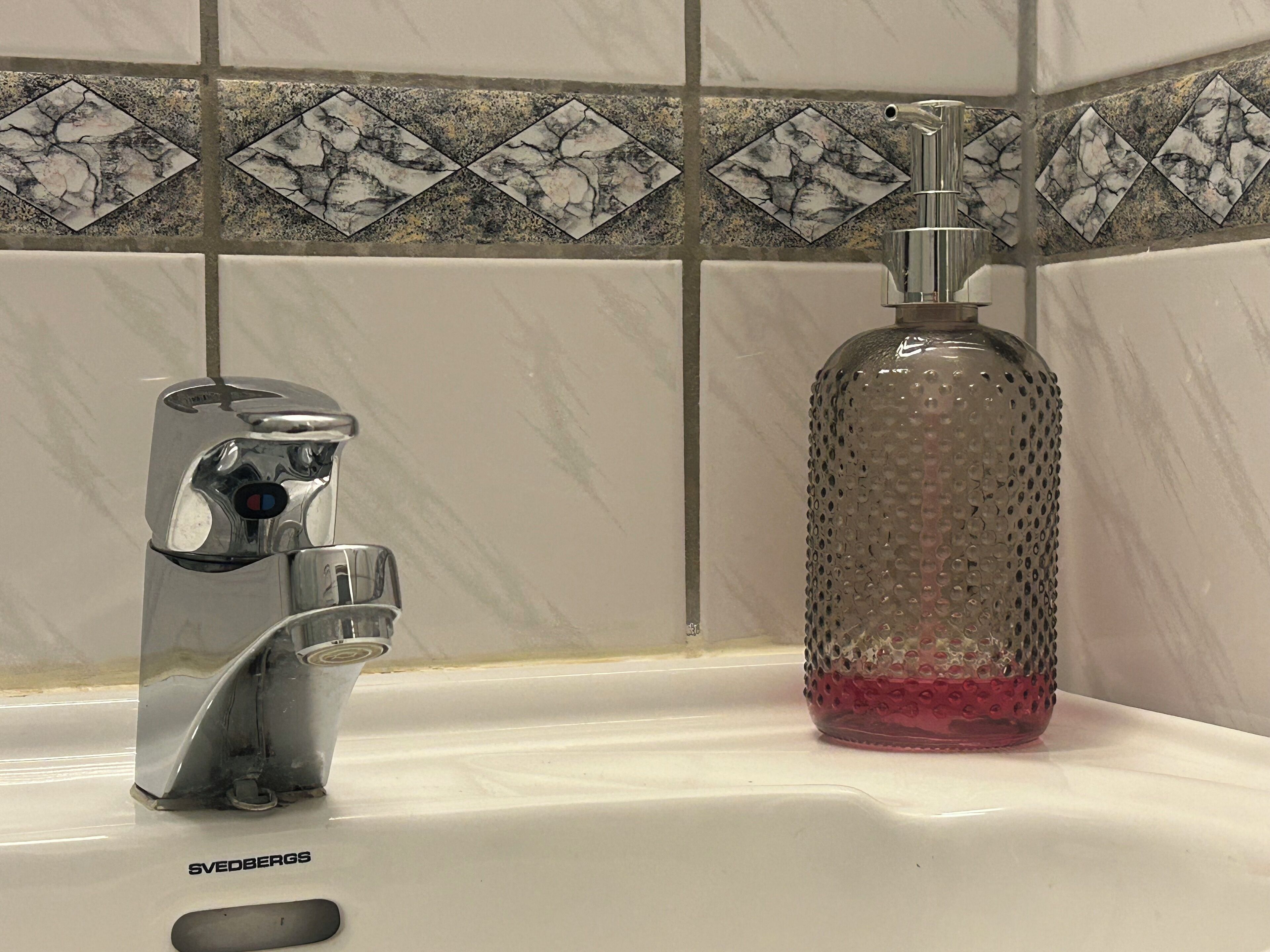 A bathroom with a white sink, a chrome faucet, and a textured glass bottle.