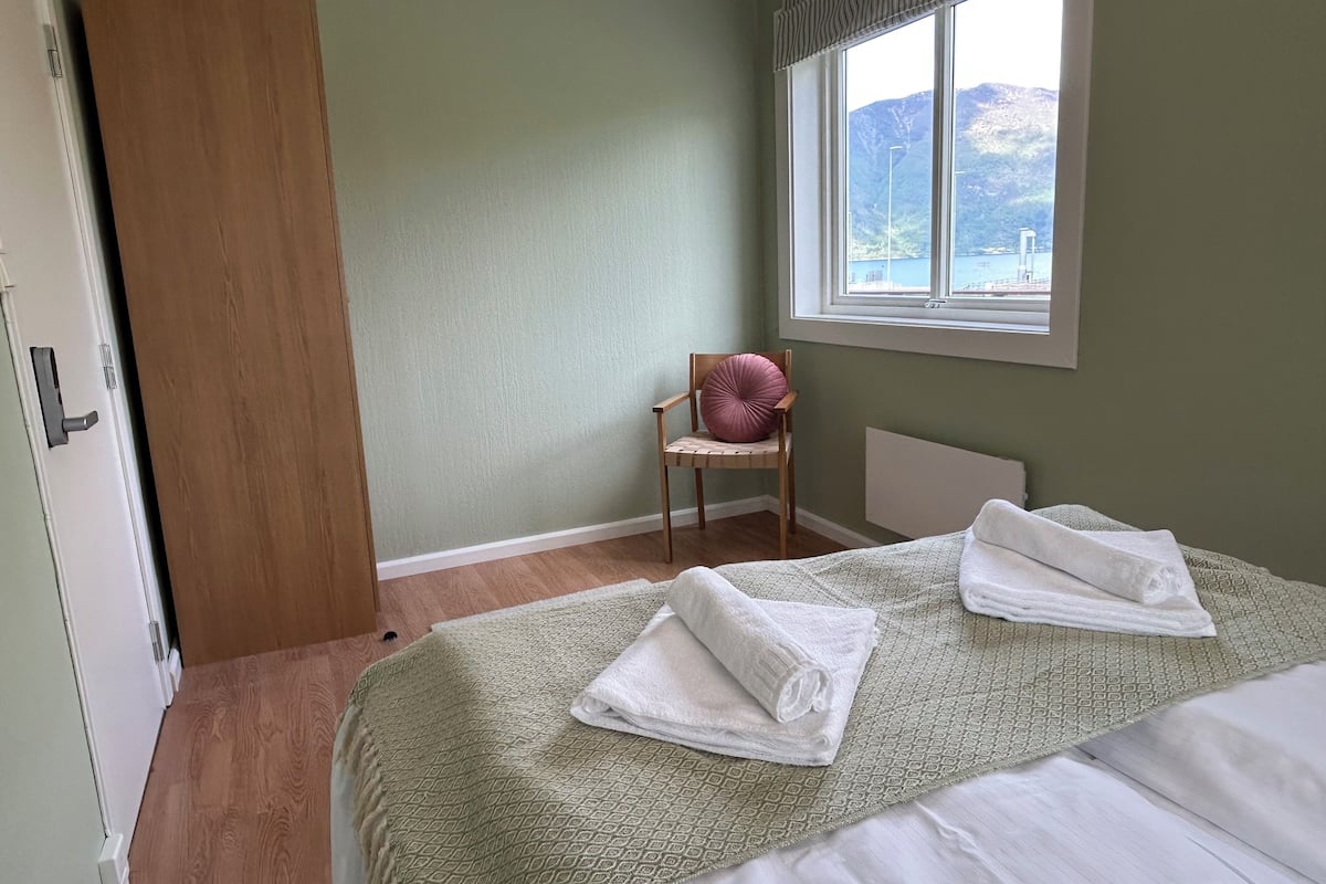 A bedroom with a bed, a chair, a window with a view, and a door.