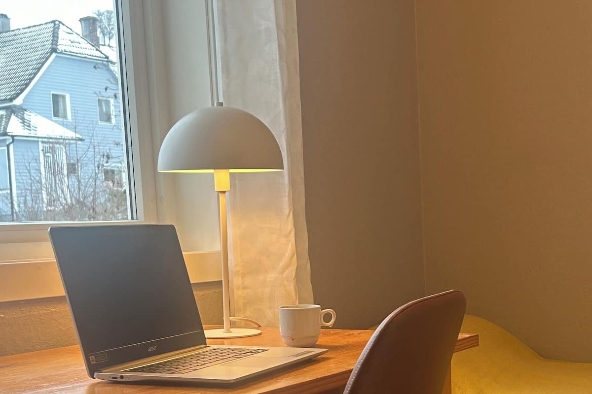 A wooden desk with a laptop, a white mug, and a lamp.